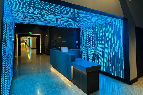 Modern cybersecurity reception desk featuring cyan backlit perforated wall and ceiling panels displaying a digital matrix dot pattern.
