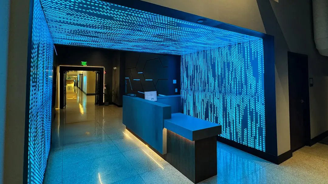 Modern cybersecurity reception desk featuring cyan backlit perforated wall and ceiling panels displaying a digital matrix dot pattern.