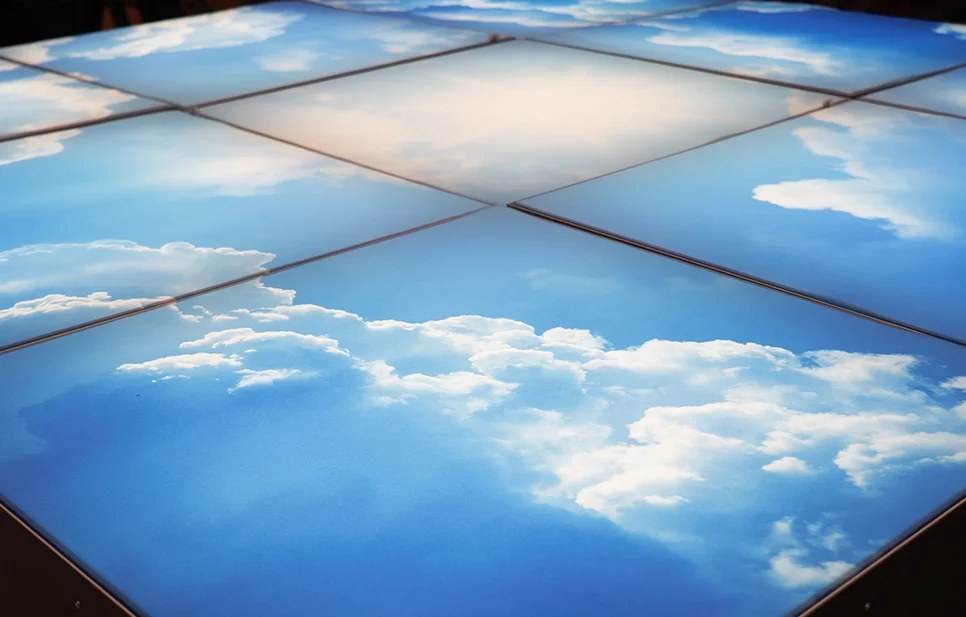Modular grid of backlit lightboxes featuring a printed graphic of a vibrant blue sky with soft white clouds.