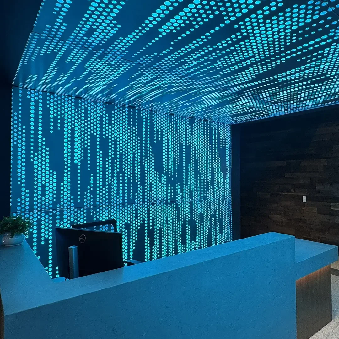 Modern cybersecurity reception desk featuring cyan backlit perforated wall and ceiling panels displaying a digital matrix dot pattern.